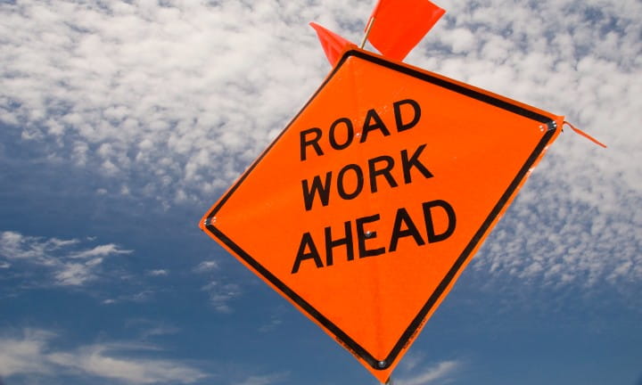 Road work ahead sign against a blue sky with clouds.