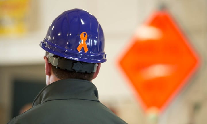 A male worker with a blue hard hat and an orange ribbon sticker showing support for those worker who have died in work zones.