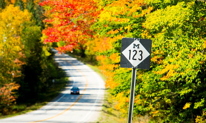A red sports car drives past the Good Hart General Store on M-119 Tunnel Of Trees in Emmet County.