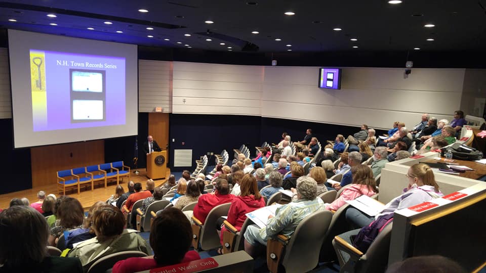 A crowd of people in sitting and watching a presentation.