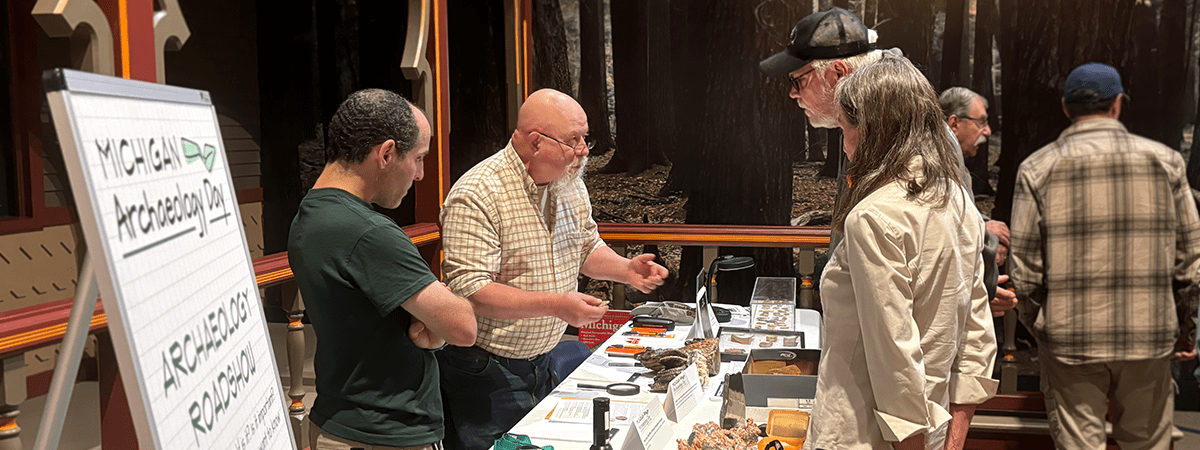 Two people standing at a table talking to exhibitors at Archaeology Day.