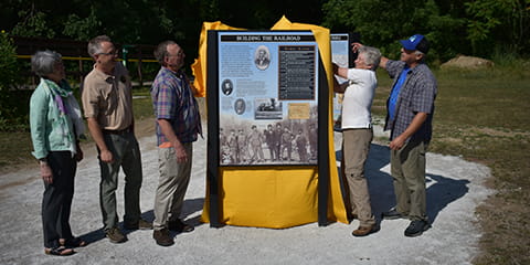 A group of people lift a yellow cloth off a large sign.
