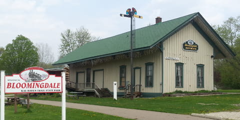 Exterior view of cream-colored historic depot shows many large outdoor artifacts