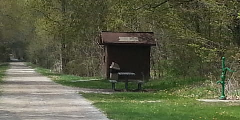 Rustic restroom and water pump near trail; close by, a trash receptacle and picnic table