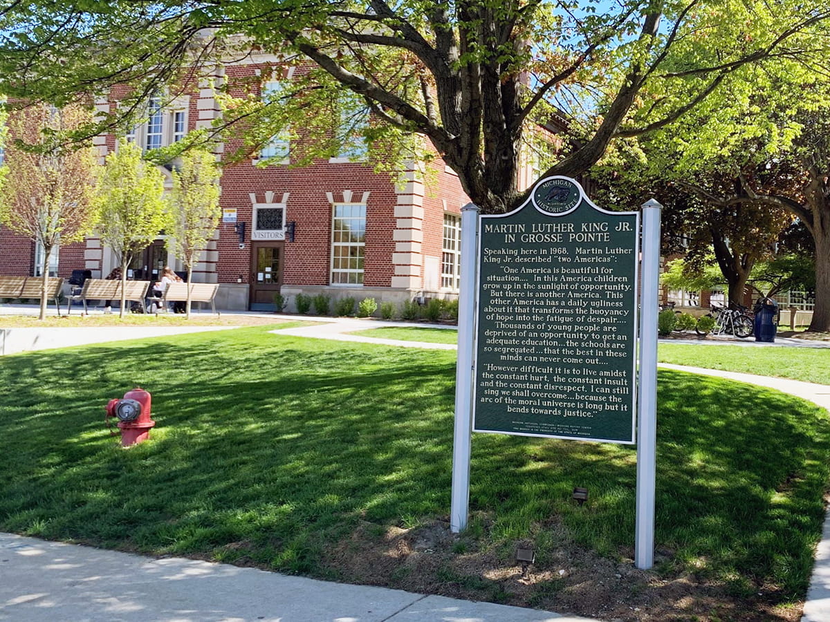 The MLK Jr. in Grosse Pointe historical marker stands near a brick-and-stone building 