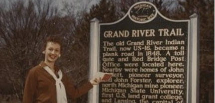 A woman gestures to a historical marker for the Grand River Trail. 