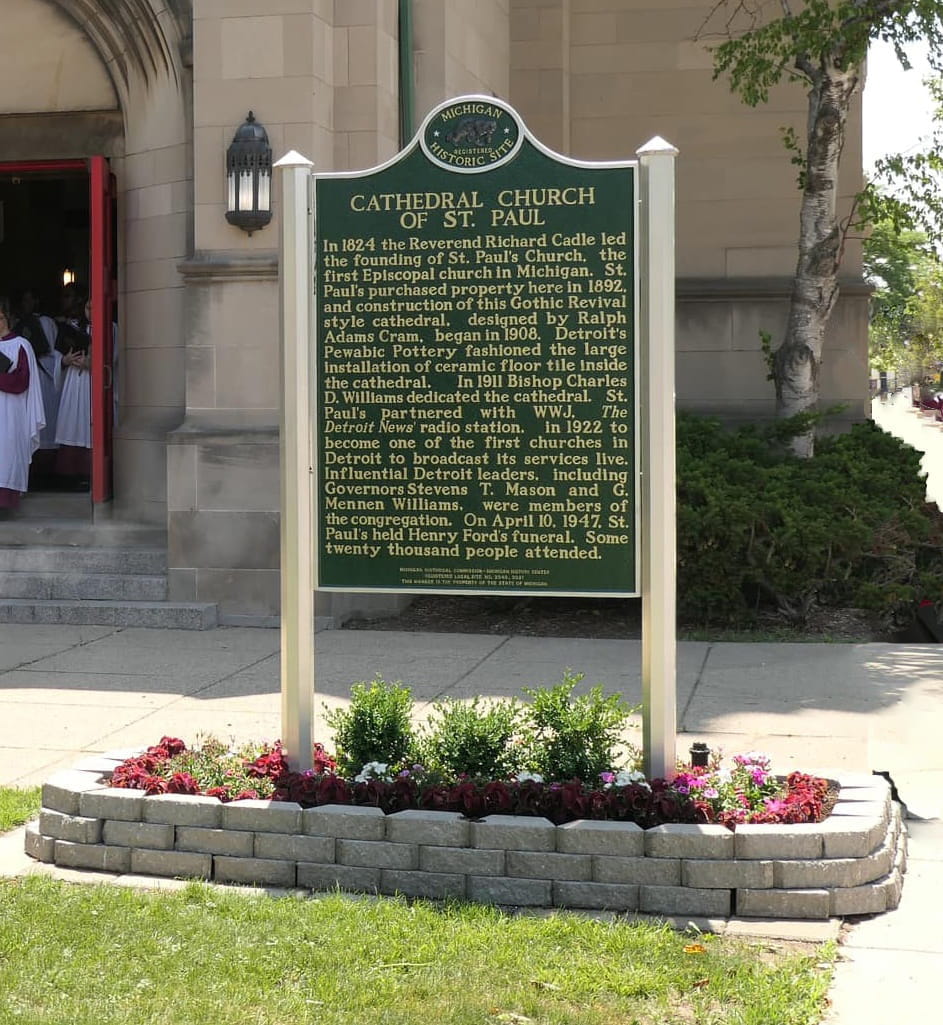 Green historical marker of the Cathedral Church of St. Paul in a small garden surrounded by plants.