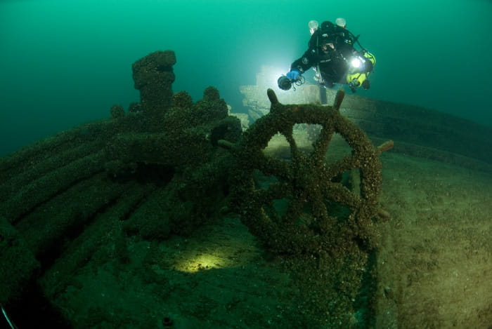 A diver shines a flashlight over a shipwreck