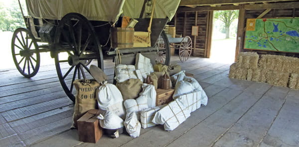 Bulap bags and cloth-wrapped packages on the ground in front of a covered wagon