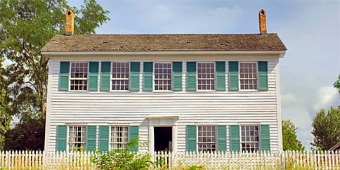 A two-story white New England saltbox-style building with green shutters and a cedar shake roof.