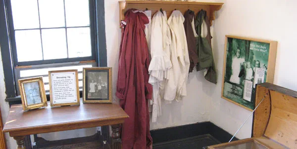Smocks and aprons hang from hooks in the corner of a room.