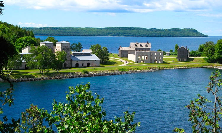 Viewed from above, several historic buildings sit on a strip of land between two bodies of water.