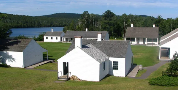 Viewed from above, six white one-story buildings a placed frame a large square green space.