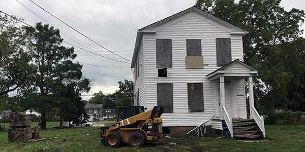 A two-story clapboard home with freshly painted white walls and boarded windows. 
