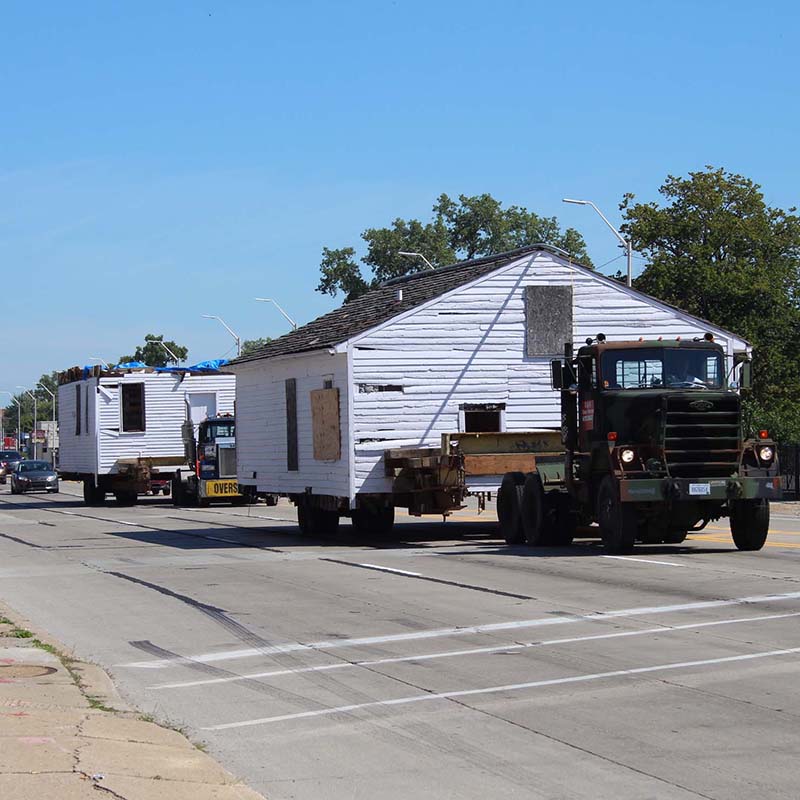 a two-story home is moved on two large trucks - one story on each - down a busy urban street.