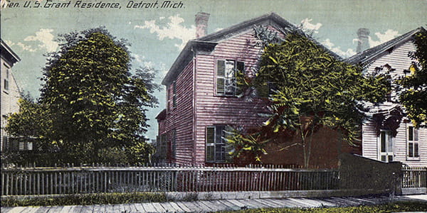 A postcard shows a pink-hued two story clapboard home. A bush obscures most of the home's front.