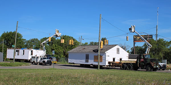 Two crewmen lift traffic lights in order for the home, loaded onto trailers, to pass underneath.