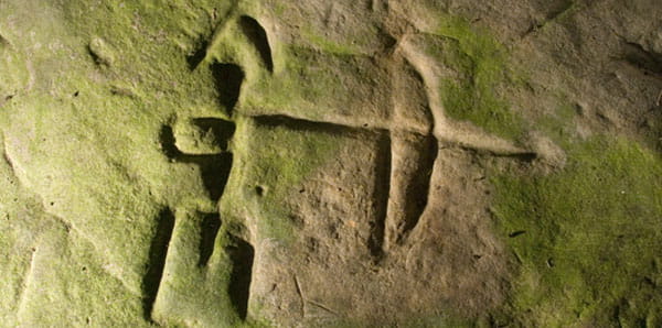 An etching in rock of a stick figure holding a bow and arrow. 