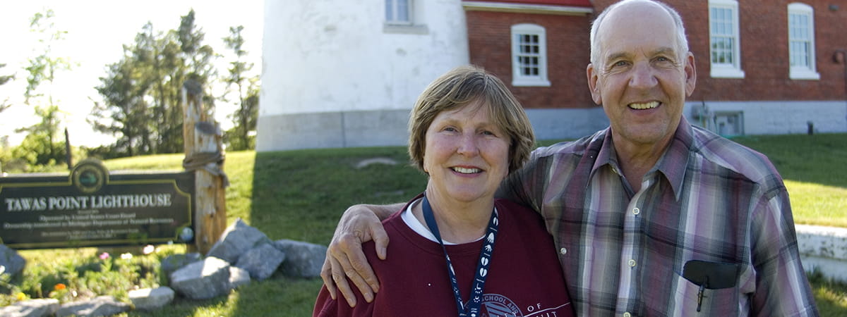lighthouse keepers pose in front of Tawas Lighthouse on a sunny summer day.