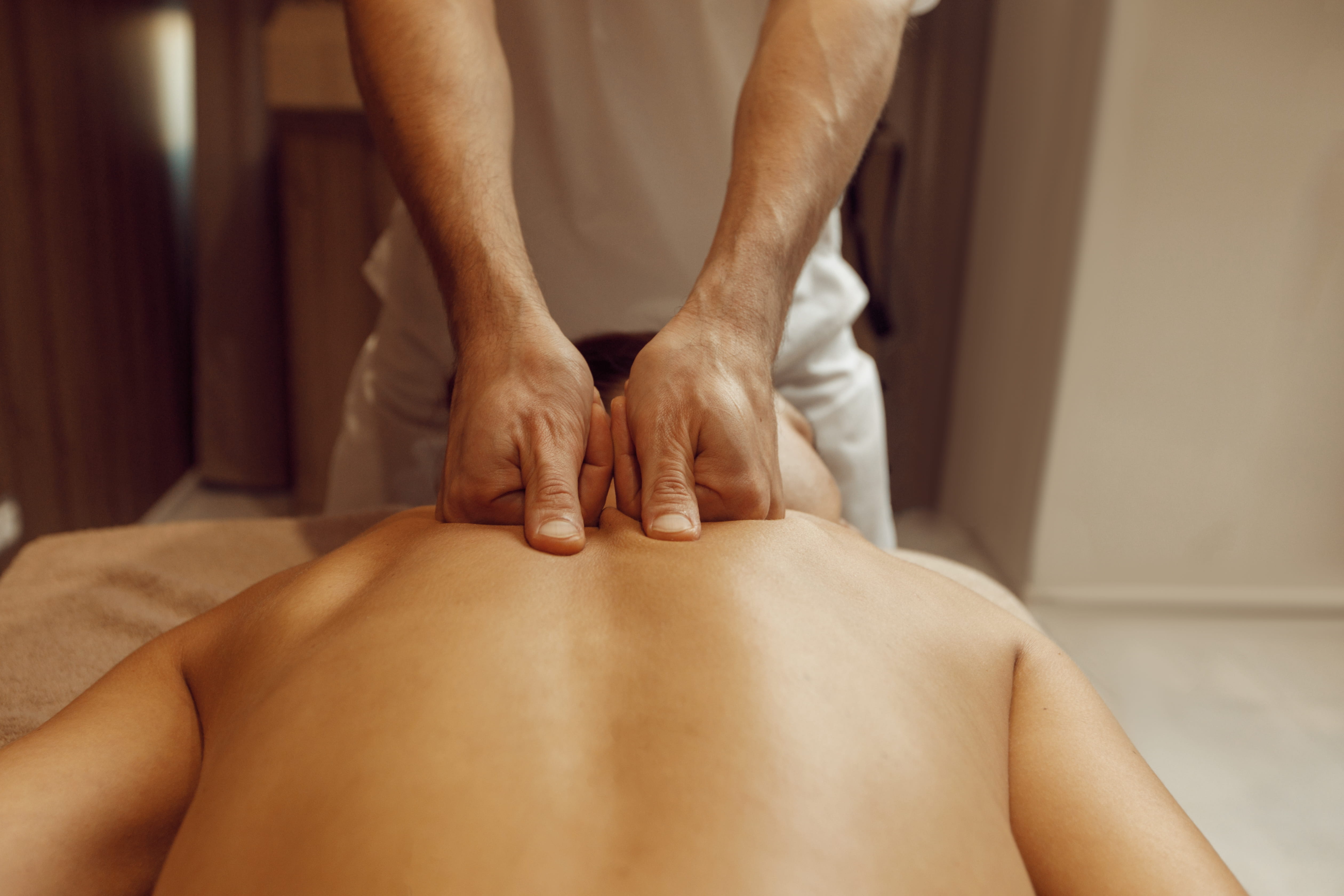 Male masseur rubbing back to slim woman, massage.