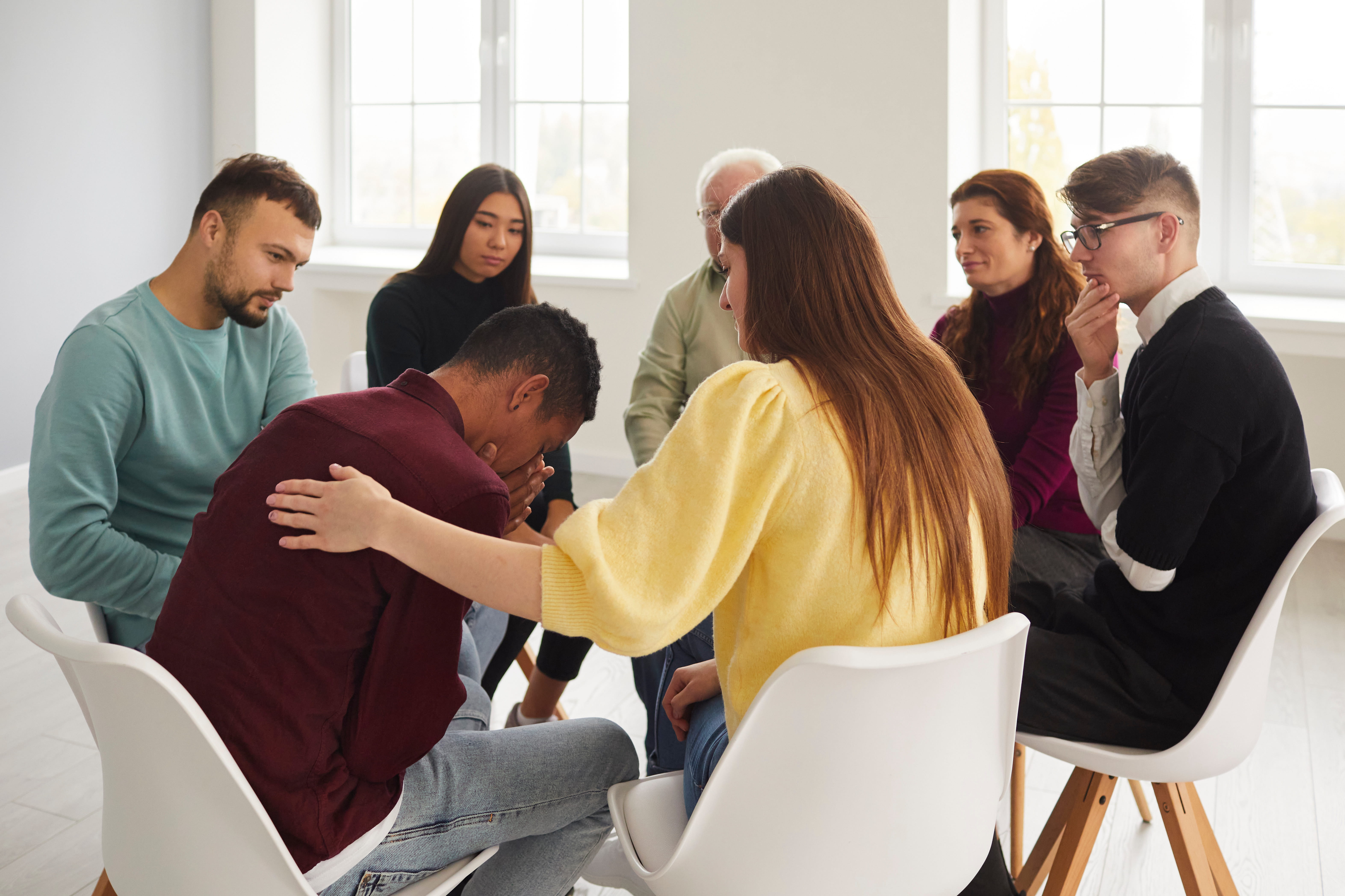 Diverse people supporting and comforting crying young man in group therapy session.