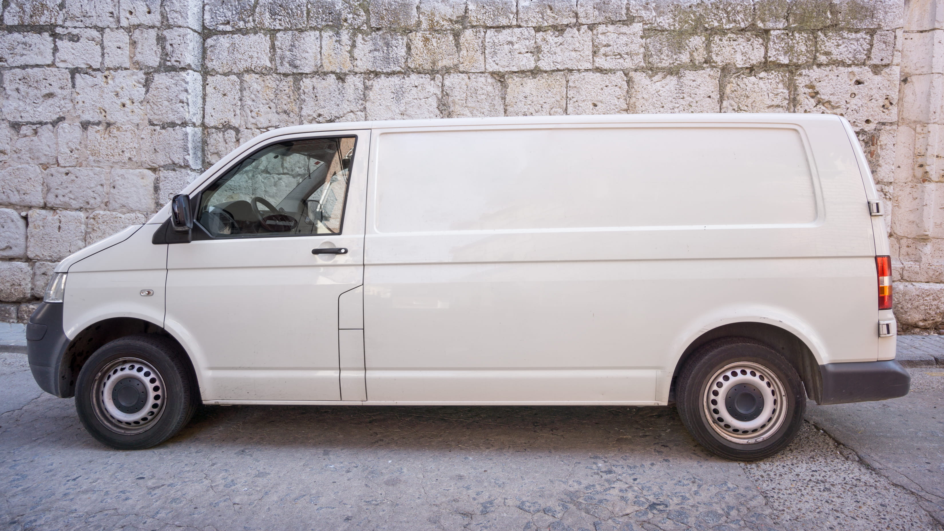 Van parked near old stone wall, side view.