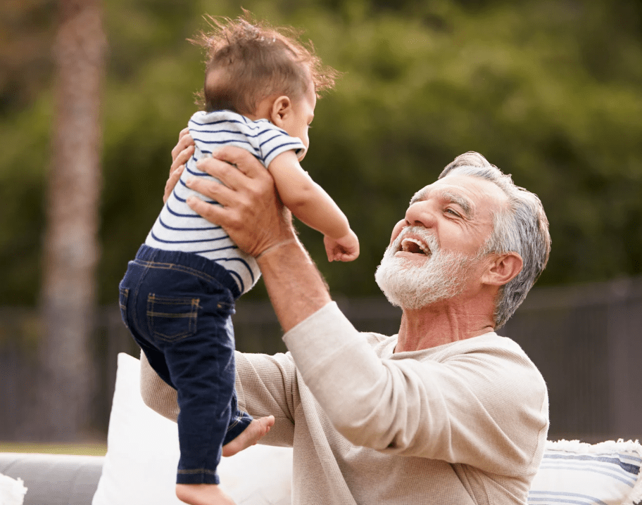 caregiver holding baby in the air and smiling