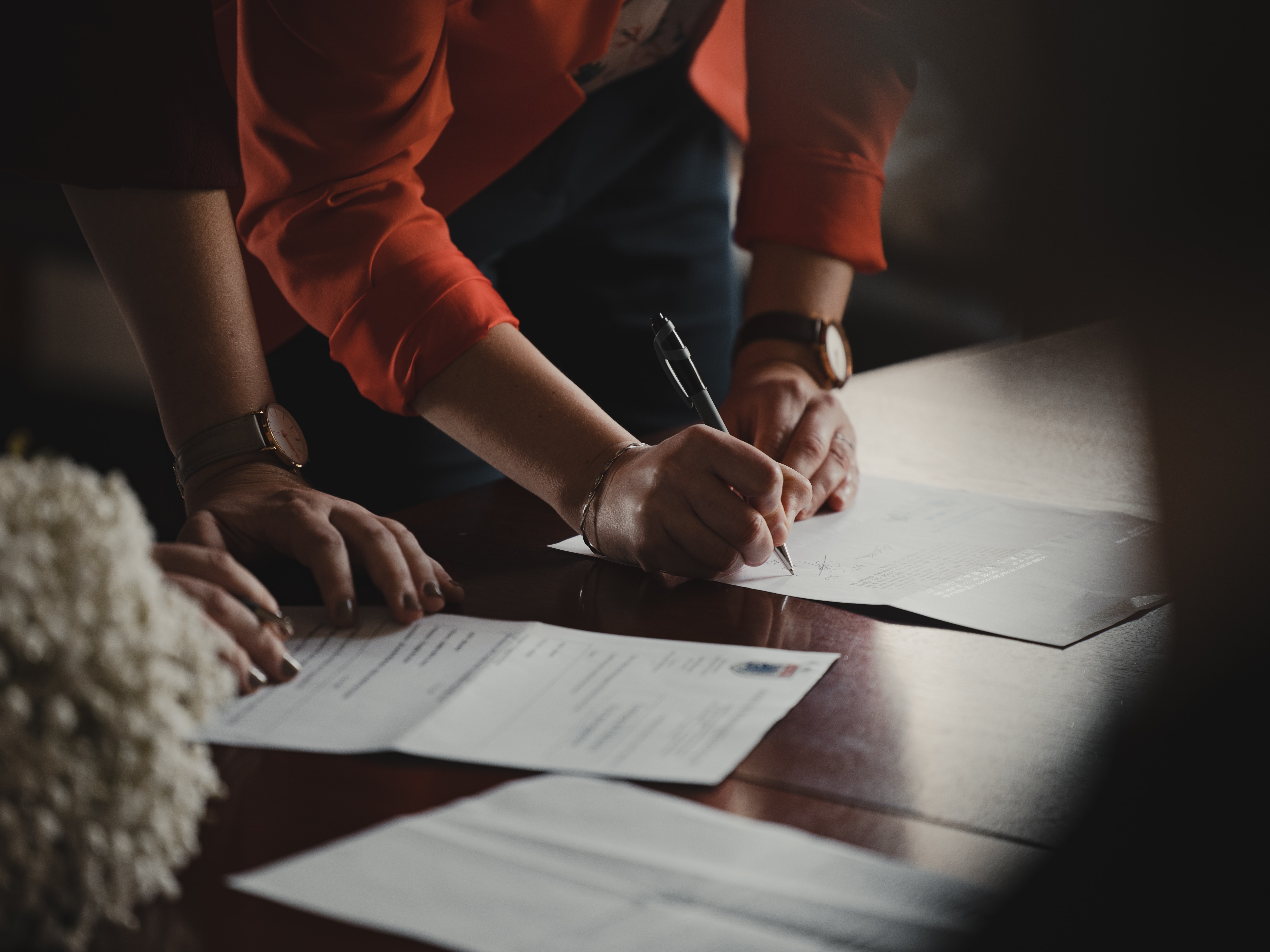 A person leaning forward over a desk signing a document.