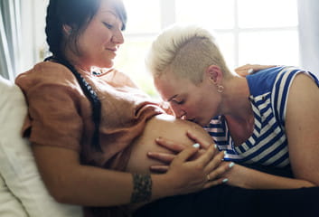 Two female celebrating pregnancy. One is pregnant and the other is kissing her tummy. 