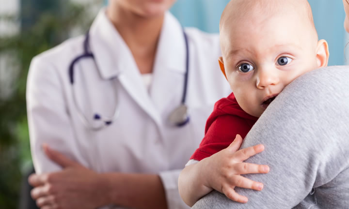 parent holding a bright eyed baby in front of doctor
