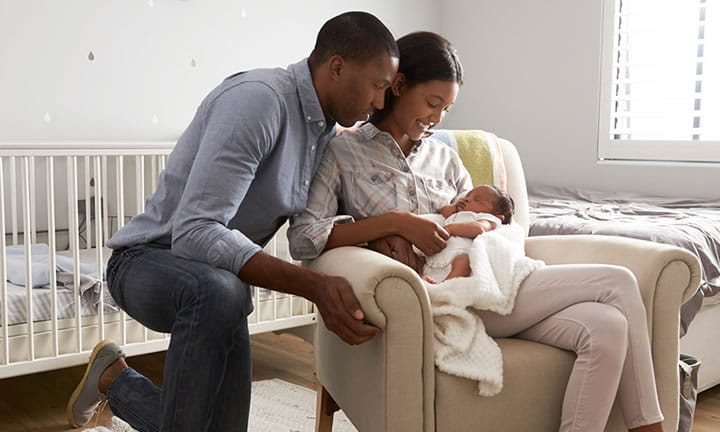 mom in chair holding baby while dad kneels next to her