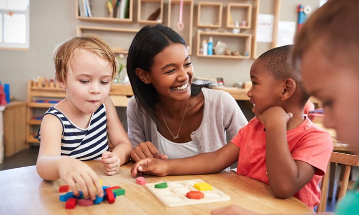 provider in care center at table with three preschoolers playing with blocks