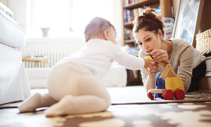 mom holding toy out to baby