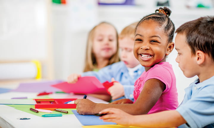 four preschoolers in classroom at table with one girl with big smile