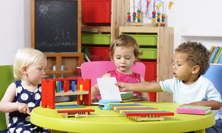 three toddlers in child care setting sitting at a table playing with toys and books