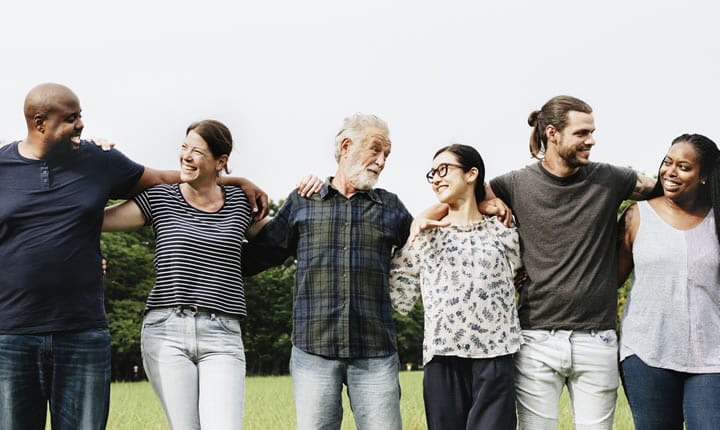 Group of adults shoulder to shoulder with arms around shoulders smiling and talking