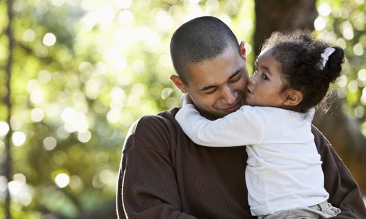 toddler daughter kissing dad while he holds her