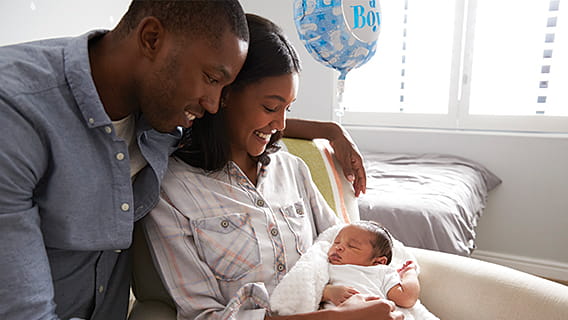 mother holding and smiling at newborn as dad holds arm around her and looks over her shoulder at baby