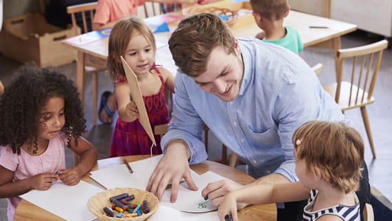 teacher drawing with children at table in child care setting