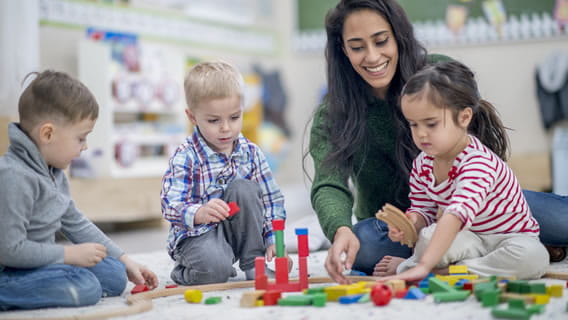 three toddlers and provider sitting on the floor playing with blocks in a care setting