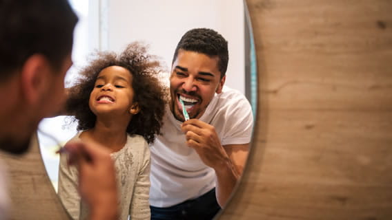 father and young daughter brushing teeth in a mirror