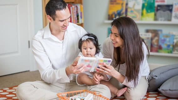 mom and dad sitting on the floor holding and reading to infant