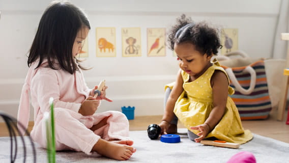 two toddler girls sitting on the floor and playing together in a care setting