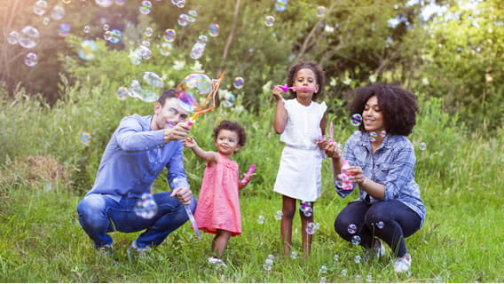 dad mom outside with toddler and preschool daughters playing with bubbles