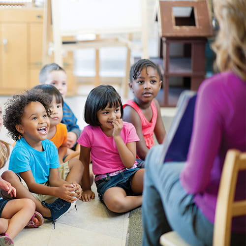 children sitting on floor in care setting listening to provider read 