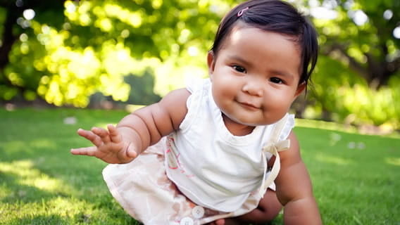 baby crawling in grass reaching out with one hand