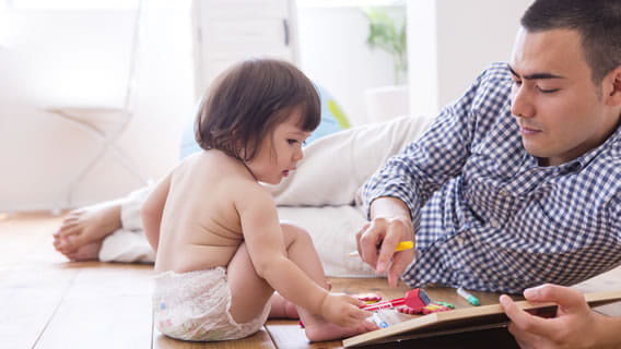 dad laying on floor propping up mini dry erase board while infant writes on board