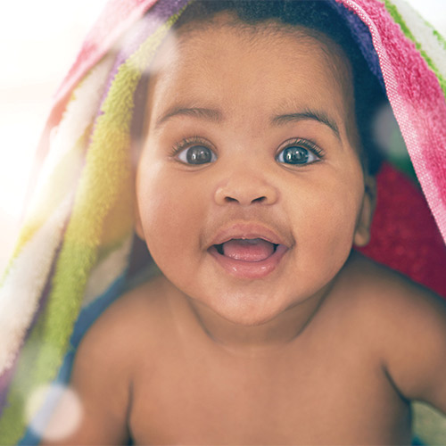 baby smiling with multicolored blanket on head