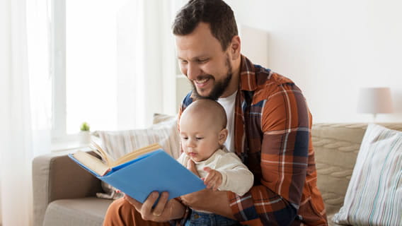 dad on couch holding and reading to baby