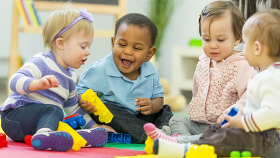 two babies playing with toys together in care setting